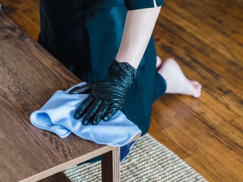 Professional cleaner wiping a wooden table with a microfiber cloth.