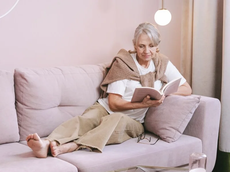 Senior woman relaxing on a sofa while reading a book at home.