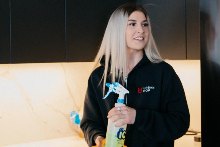 UrbanMop residential cleaner holding cleaning supplies in a kitchen