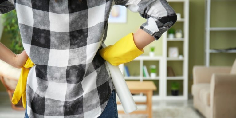A person with hands on hips, standing in a living room, deciding where to clean first.