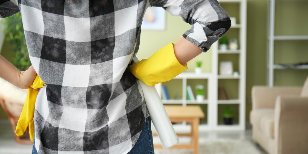 A person with hands on hips, standing in a living room, deciding where to clean first.