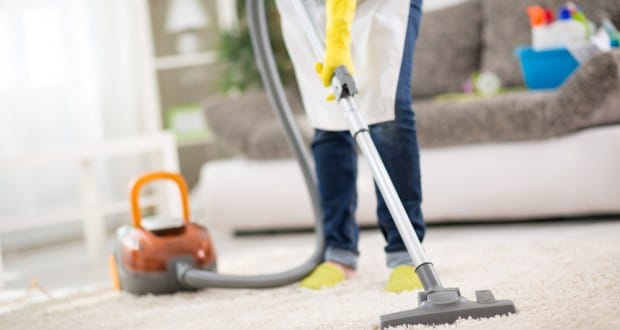 Vacuuming a light-colored carpet in a living room as part of a deep home cleaning.