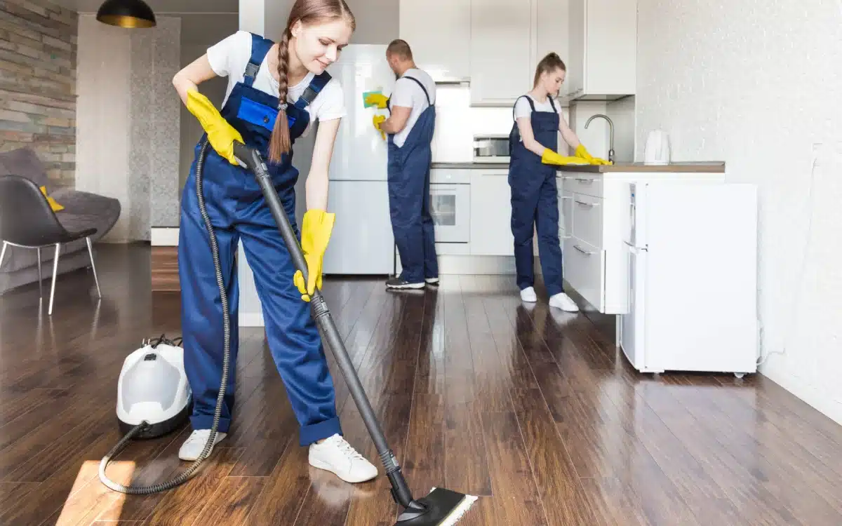 Residential cleaners vacuuming and wiping kitchen surfaces in a home.