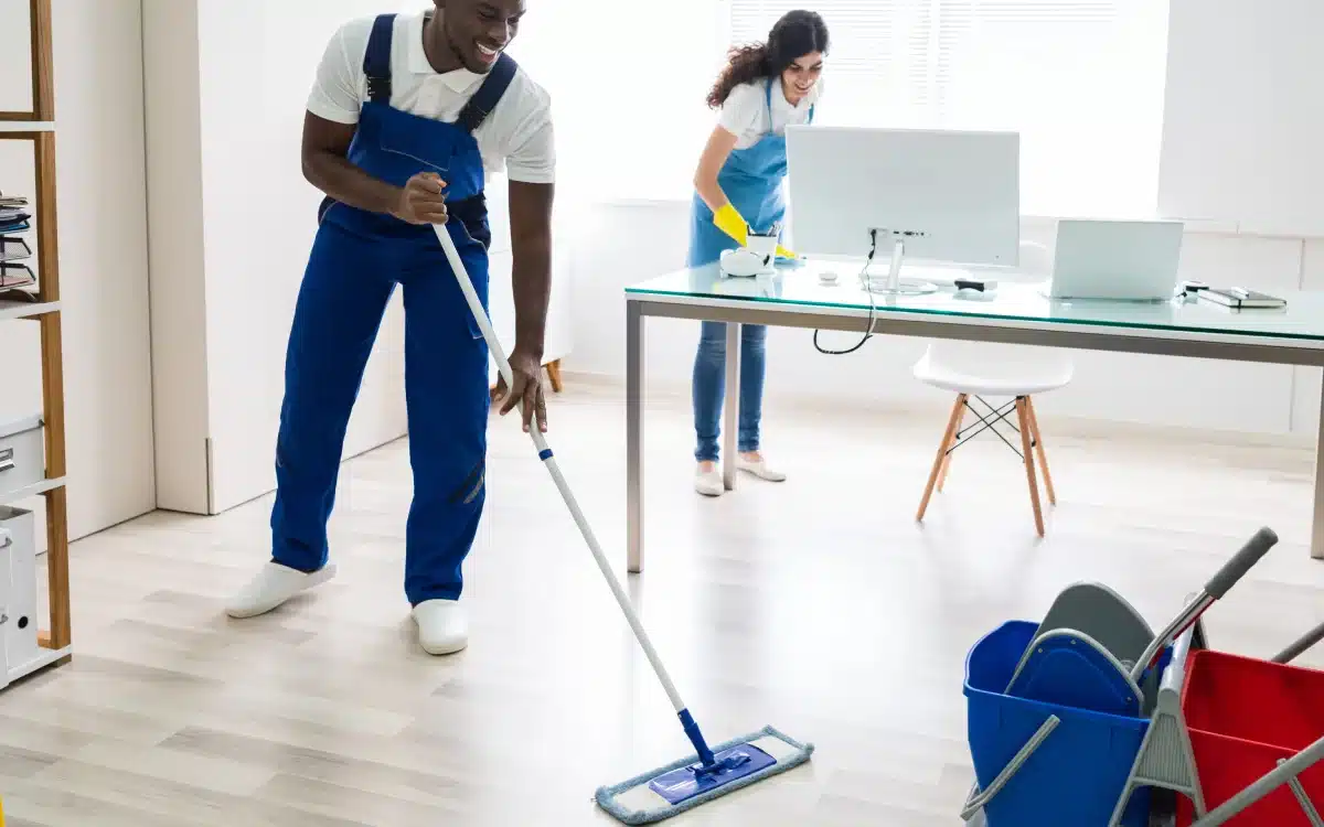 Housekeeping staff mopping office floor and cleaning surfaces.