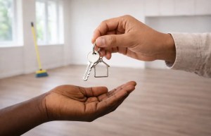 Hand passing apartment keys to another person in an empty, clean room.