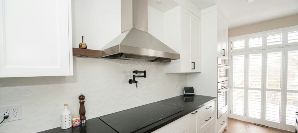 Bright white kitchen with stainless steel range hood and black countertop.