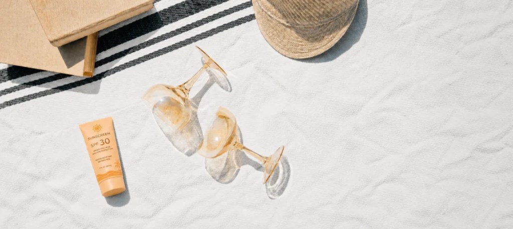 Orange sunscreen bottle and summer accessories arranged on a white towel.
