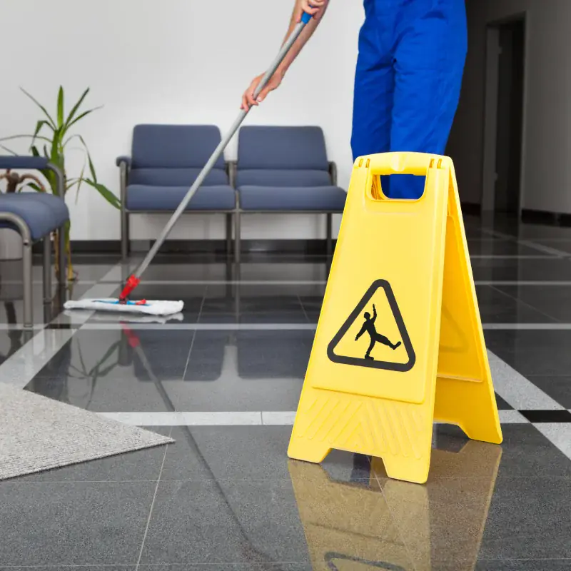 Professional cleaner mopping an office floor near a caution sign